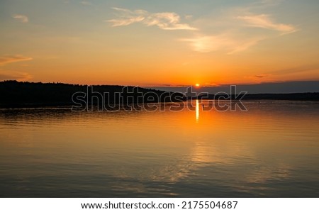 Summer evening. Sunset over the river. The sun is almost hidden behind the clouds creeping along the horizon. A golden path stretched across the water, reflecting the sunlight. 商業照片 © 
