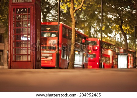 Typical London scene at night with phone booth in front and double deckers in background. Short depth of field, focus on phone booth.