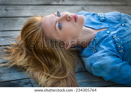 red-haired girl with bright blue eyes lying on a wooden pavement and looks at the sky. outdoor shooting.