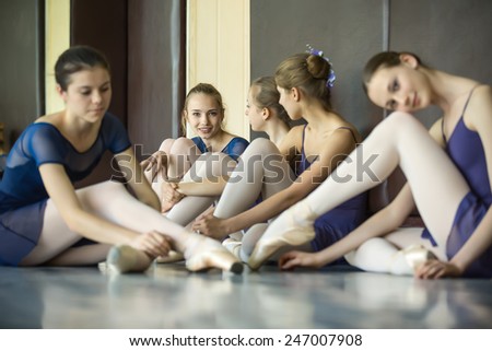 Five young dancers in the same dance costumes, resting sitting on the floor. Dance Class. Ballet School. Discussions yet with each other.
