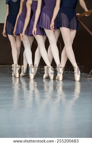 Five ballet dancers in class near the handrail, legs only. Model wearing white tights.