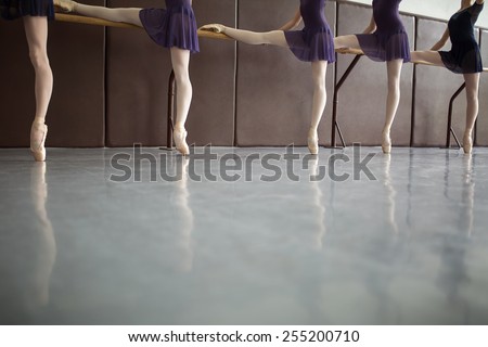 Five ballet dancers in class near the barre, legs only. Model wearing white tights, with one foot resting on the bar