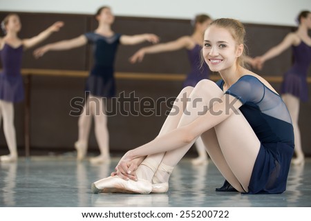 ballerina with smile sitting on the floor in a dance class dancers practicing on the background