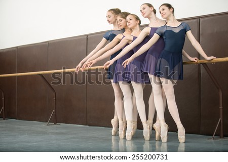 Five ballet dancers in class near the barre. Model wearing white tights. Girls look toward
