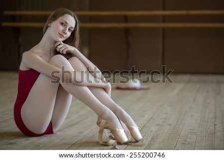 Portrait of a young ballerina sitting on the floor in a dance class. The model looks at the camera.