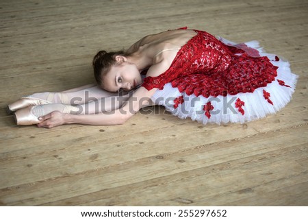 Charming young dancer doing stretching leaned over, looking at the camera. Red outfit.