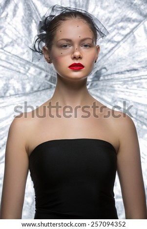 Attractive girl model with a veil on his face in black skin-tight dress on a background of silver umbrella. Umbrella - studio lighting element.