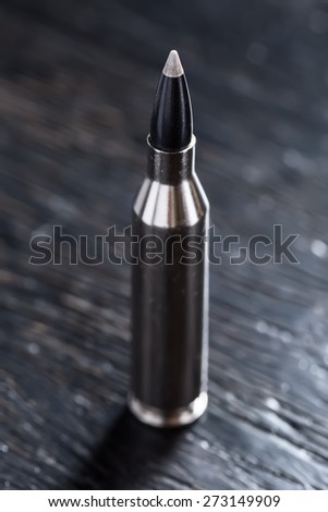 One cartridge with teflon bullet and silver sleeve on a black wooden background