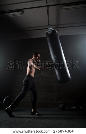 Young boxer in light weight with bare-chested in fighting stance against a dark background in the studio