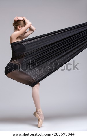 Slim dancer plays with black mesh fabric in the studio on a white background in lingerie.