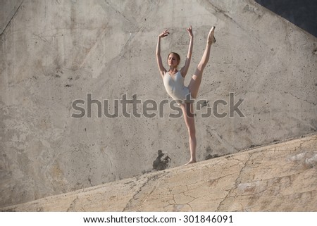 Slim dancer stands in a ballet pose on a gray urban concrete background. Outdoors shooting with sun light.