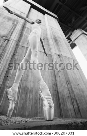 Slim ballerina on a background of the concrete pillars. Lowest point shooting wide-angle lens distorts the artistic perspective and lengthens the leg and rising dancer. Black and white photo.