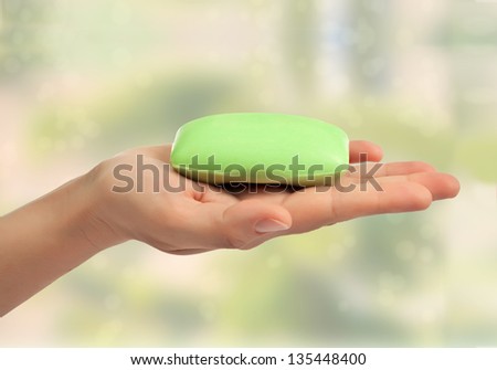 Green soap bar in hand on green abstract background.
