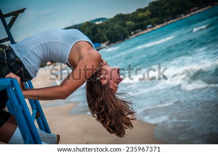 girl head thrown back sitting on the railing at the beach
