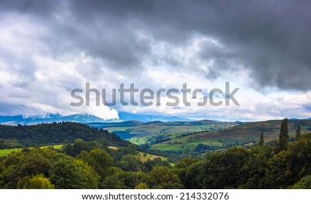 Storm clouds above mountains landscape. Green grass and trees, grey clouds