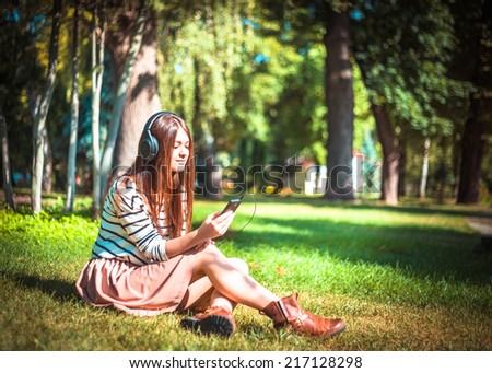Young girl listening to music in park. Student girl outside listening to music on headphones. Happy young teenager student of Caucasian ethnicity