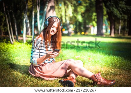 Young girl listening to music in park. Student girl outside listening to music on headphones. Happy young teenager student of Caucasian ethnicity