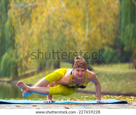 Young woman doing yoga in autumn park near lake