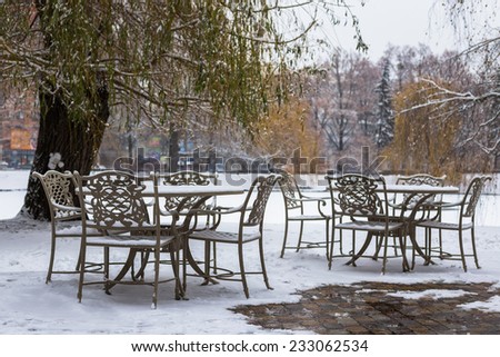 Round tables and forged chairs with first snow in city cafe