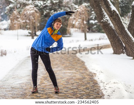 Athlete woman doing exercises during winter training outside in cold snow weather in park