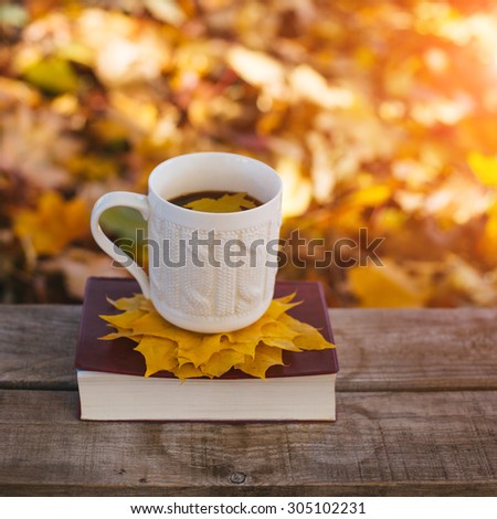 Hot coffee and book with autumn leaves on wood background - seasonal relax concept