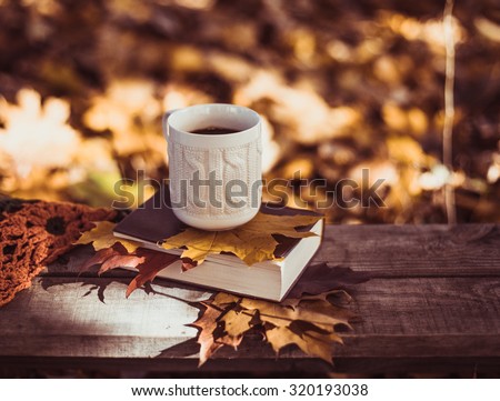Hot coffee and red book with autumn leaves on wood background - seasonal relax concept