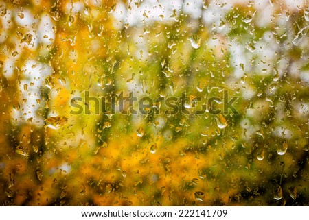 Raindrops on dirty window with out of focus autumn landscape in background
