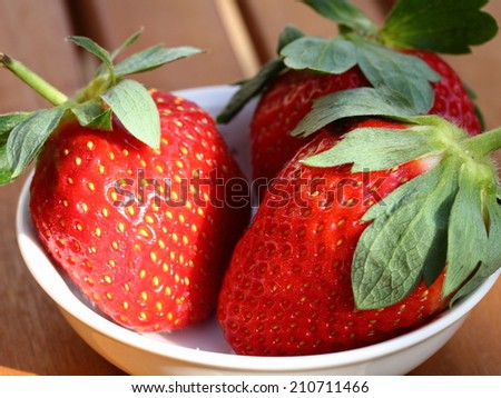 group of fresh red strawberry in a white bowl on the outdoor table in the morning