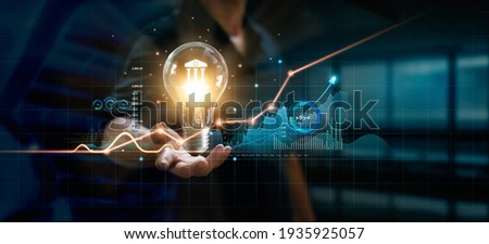 Businessman holding creative light bulb with growth graph and banking icons. Financial innovation technology develop new products and services that enhance successful and profit in global business.