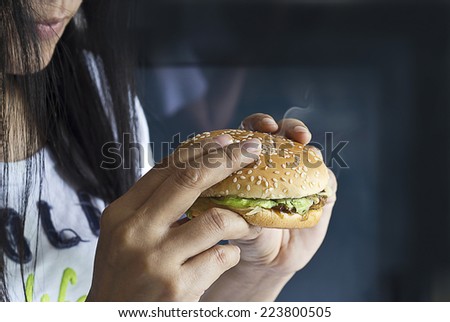 Women see hamburger in hand on dark background, junk food concept