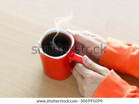 Red coffee cup with smoke in woman hand on wooden table