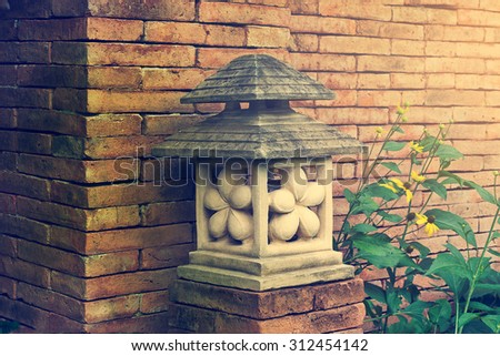 Japanese garden stone lantern lamp it around the flowers grow on brick wall background