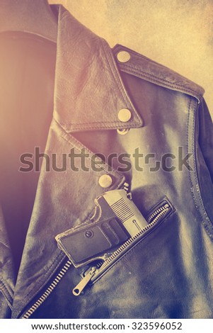Vintage old leather jacket with gun in the pocket on grain paper background