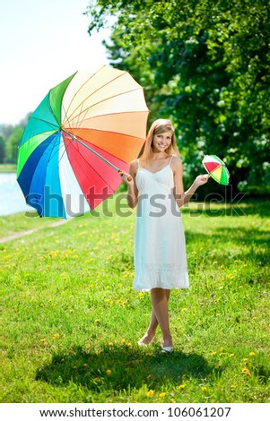 Smiling woman chooses big or small rainbow umbrella outdoors