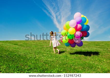 Happy little girl holding colorful balloons. Child playing on a green meadow. Smiling  kid.