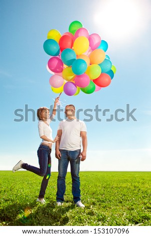 Couple in love with balloons in hands in the field against the sky in the green garden.