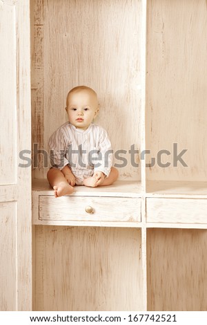 Beautiful little baby sitting in the closet. Smiling child and interior of a bedroom. Cute kid