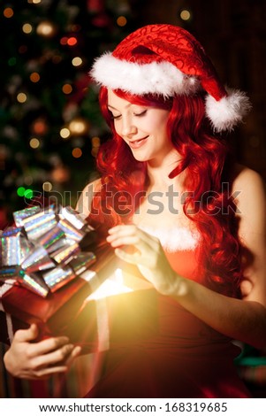 Young beautiful smiling santa woman near the Christmas tree with bunny. Fashionable luxury  girl celebrating New Year holding gift in hands
