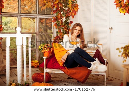 Beautiful autumn woman smiling on the porch of yellow and orange autumn leaves. Stylish autumn girl