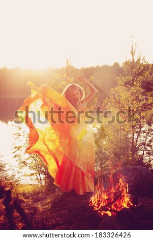Beautiful witch in the woods near the fire. Magic woman celebrating Halloween. Girl doing witchcraft in the forest.