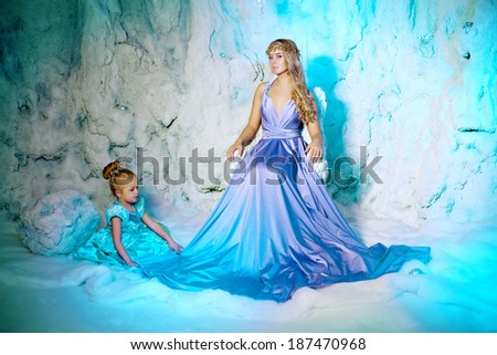 Little girl with mother in princess dress on a background of a winter fairy tale. Baby and mom snow queen. Sweet smiling child and mum snowy kingdom. Kid in in carnival costume