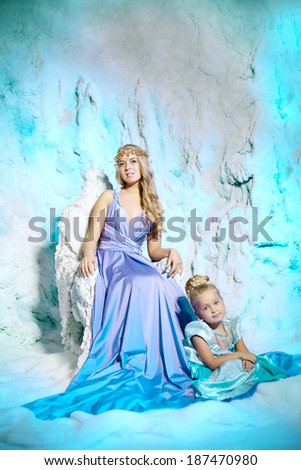 Little girl with mother in princess dress on a background of a winter fairy tale. Baby and mom snow queen. Sweet smiling child and mum snowy kingdom. Kid in in carnival costume.