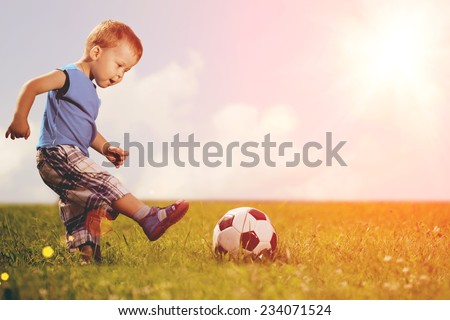 Sports kid. Boy playing football. Baby with ball on sports field. Child plays.