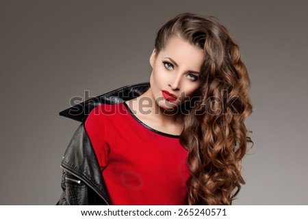 Beautiful young woman model brunette with long curled hair with red lips in leather jacket. Girl wave, curly hairstyle. Health hair shine. Beauty lady face with sexy glance.
