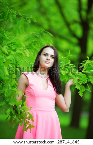 Young spring fashion woman. Trendy girl in the branches of the oak in the spring summer garden. Springtime or summertime. Lady in spring landscape background.