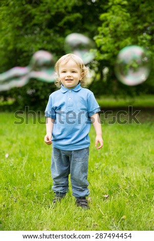 Cute curly baby with soap bubbles children playing running Child playing outdoors in the flowering trees in spring summer garden.  Springtime or summertime. Boy in spring summer landscape background.