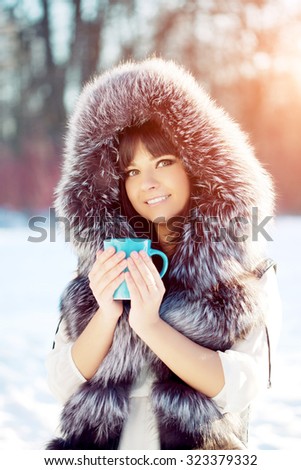 Young woman with a cup of hot drink in winter wood Winter woman on background of winter landscape sun. Fashion girl in forest wonderland. Winter sunset scene. Model in sunlight, backlight