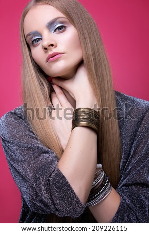 Fashion blond girl on the pink background posing with her hands silver eyeshadow silver shirt bracelets