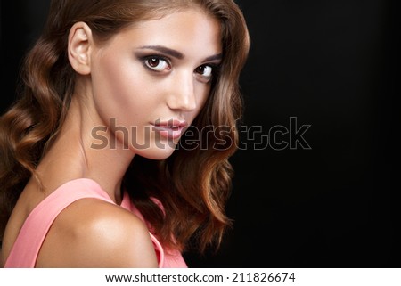 Beautiful brunette woman in a pink dress with wavy hairstyle and smoky eyes make up on black background