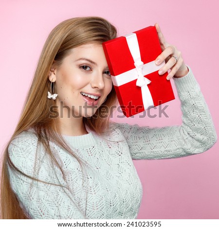 Sweet blonde woman holding small gift box with ribbon. Studio portrait over pink background. Happy birthday. Valentines Day. Joyful